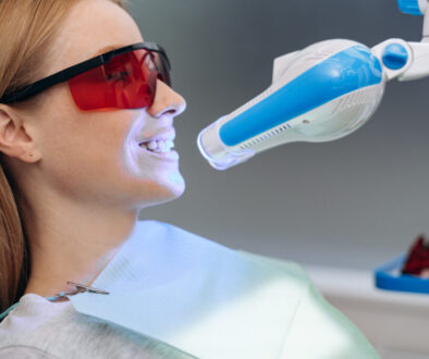 Attractive, young patient in a dental chair with goggles shows her teeth. Dental equipment shines on the patient's teeth