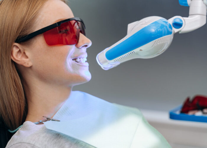 Attractive, young patient in a dental chair with goggles shows her teeth. Dental equipment shines on the patient's teeth Attractive, young patient in a dental chair with goggles shows her teeth. Dental equipment shines on the patient's teeth